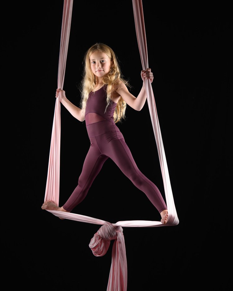 Aerial silks performer posing gracefully on burgundy silks against a dark background